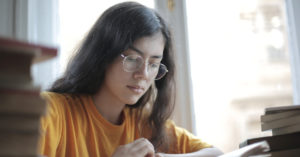 Girl with glasses preparing for the GCSE English Language exam surrounded by books